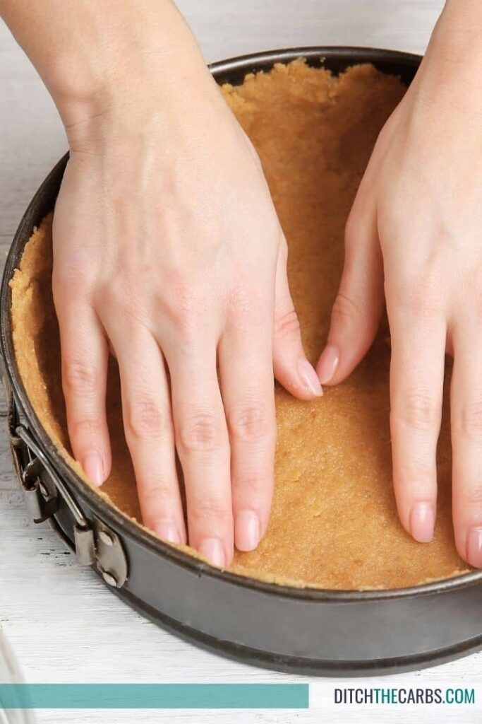 hands pressing a cheesecake crust into a lined dish