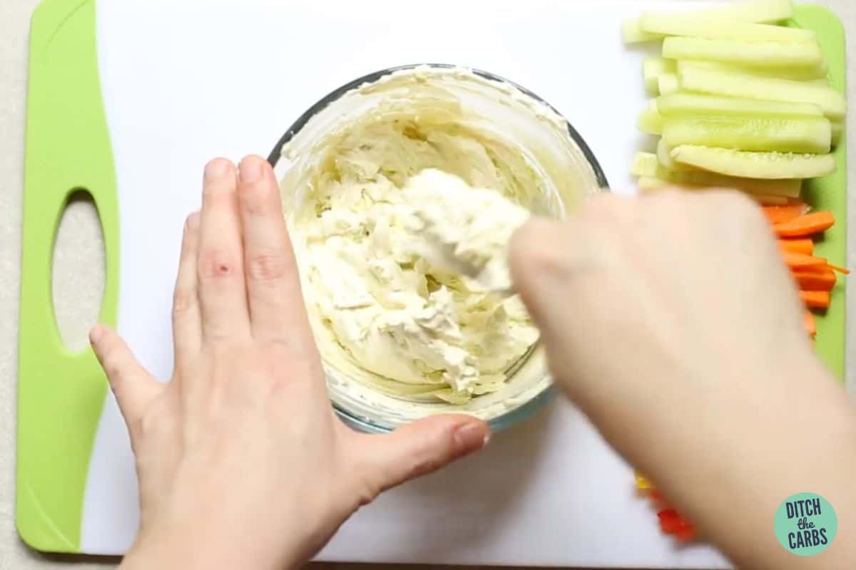 hands mixing cream cheese and avocado in a small mixing bowl