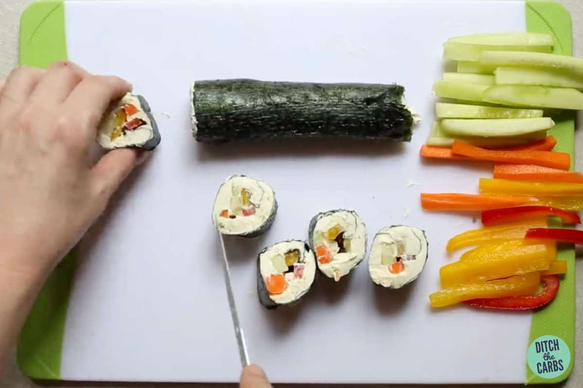 slicing keto sushi on a white chopping board