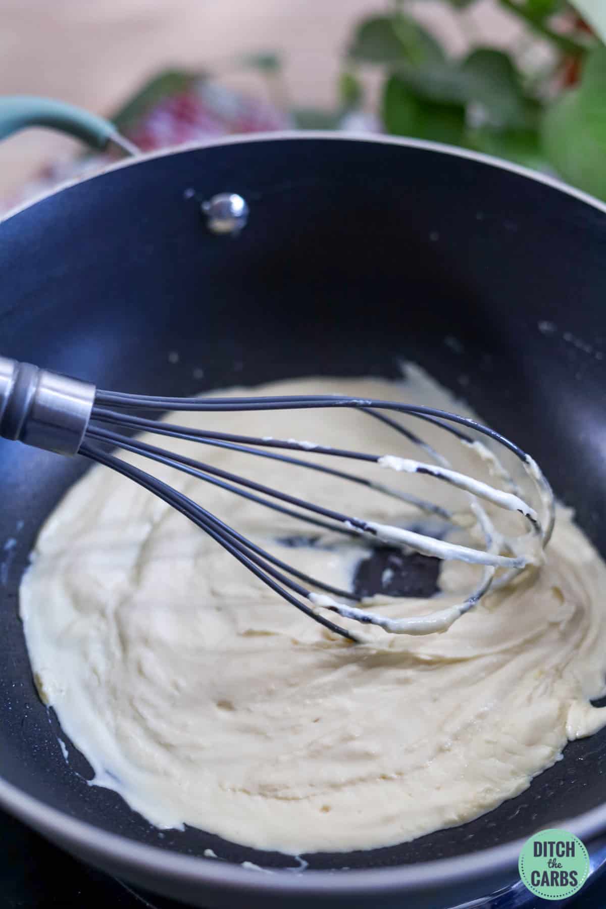 a creamy sauce in a frying pan with a whisk