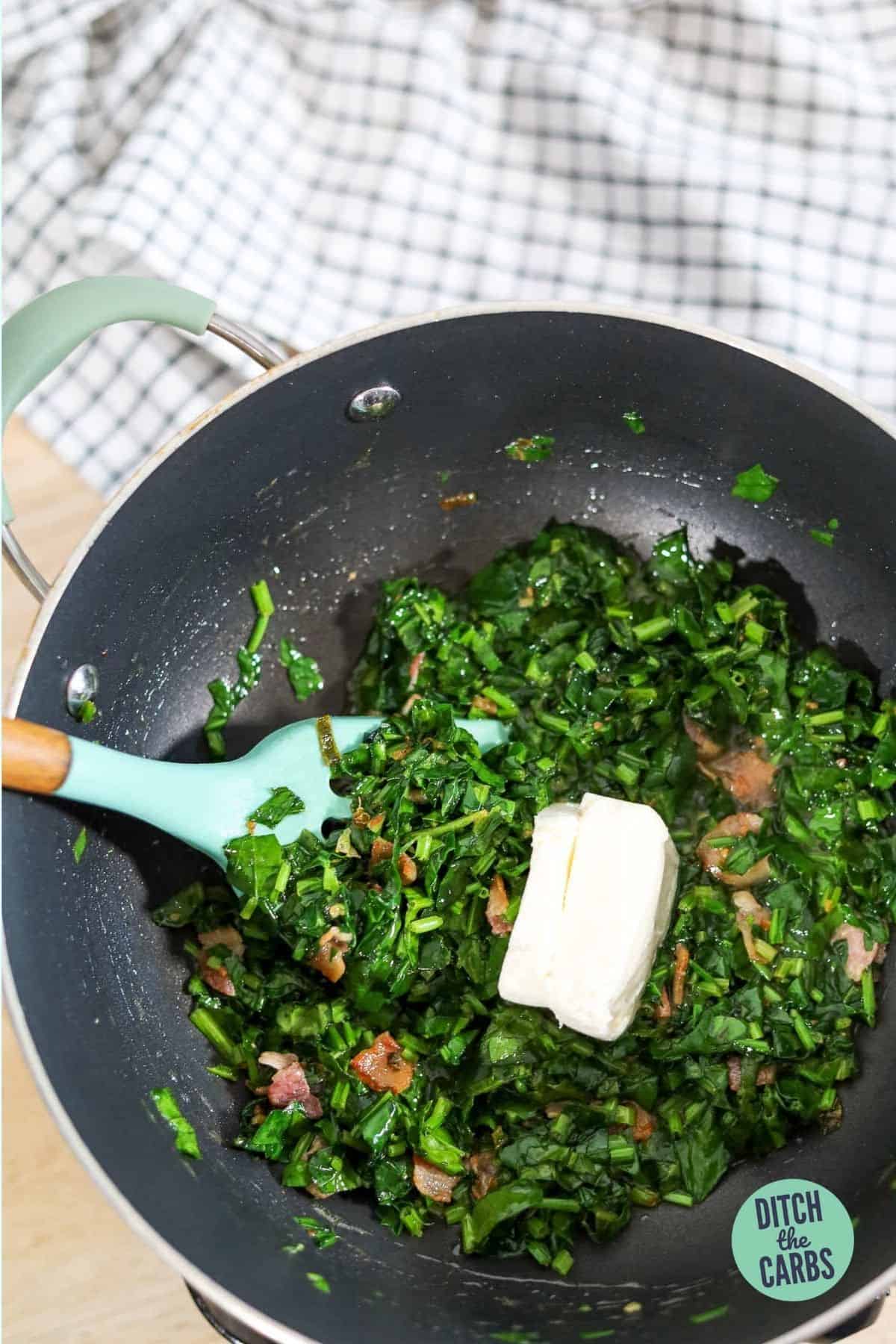 adding cream cheese to spinach in a frying pan