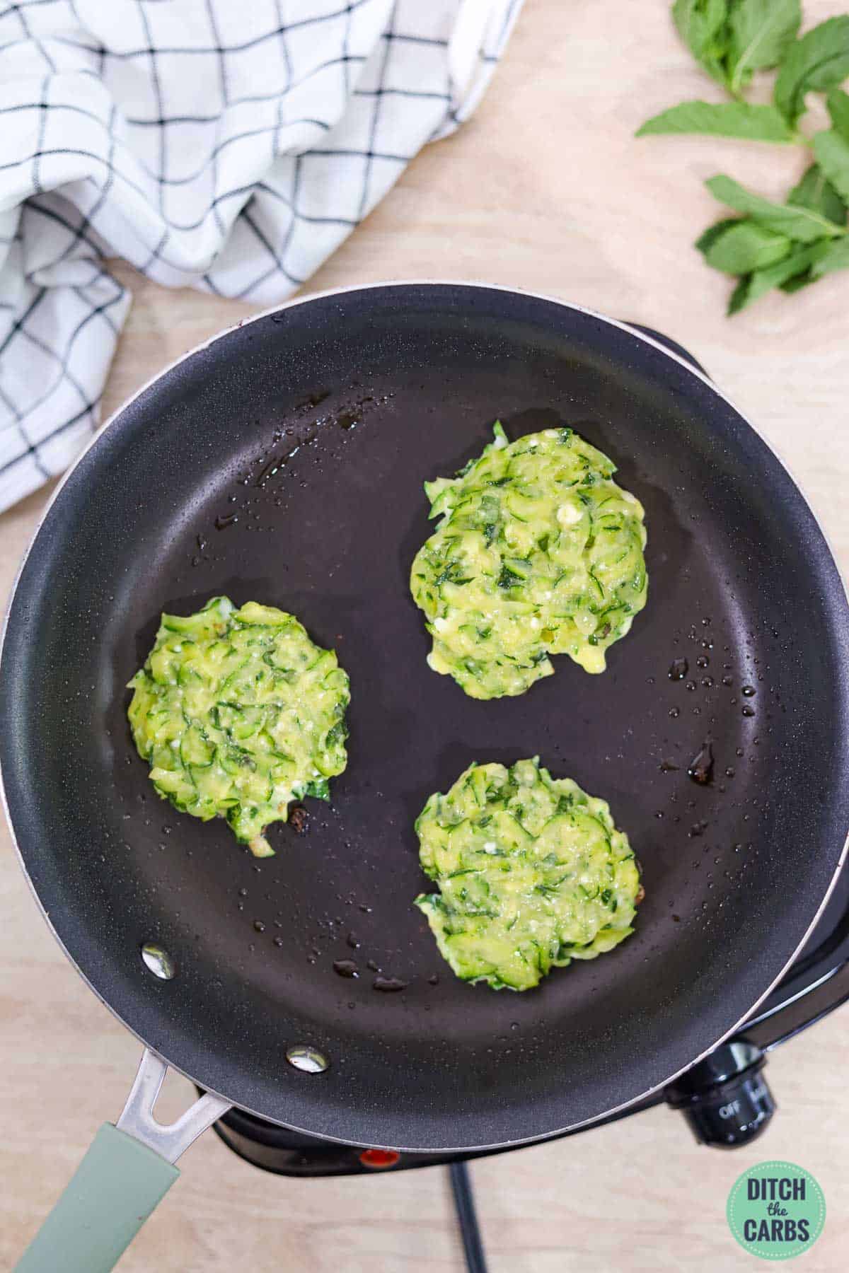 a frying pan with zucchini fritters cooking
