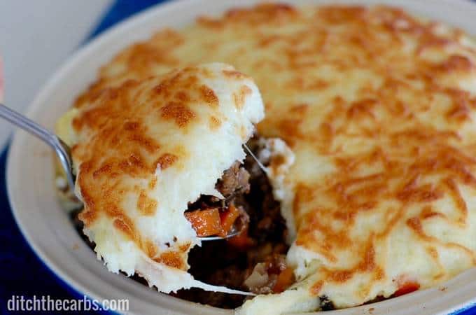 Low-carb shepherd\'s pie with a cheesy cauliflower crust being served from the baking dish