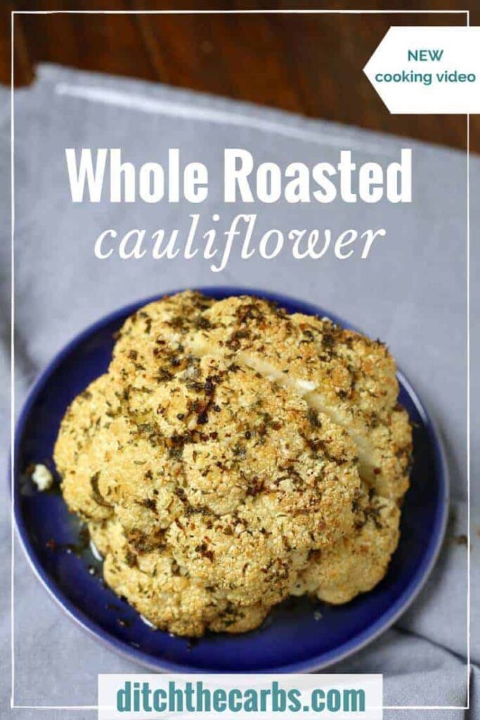 A whole roasted cauliflower brushed with butter and herbs sitting on a blue plate