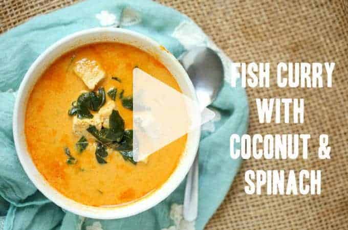 Bowl of low carb fish curry with coconut and spinach on a blue cloth and silver spoon