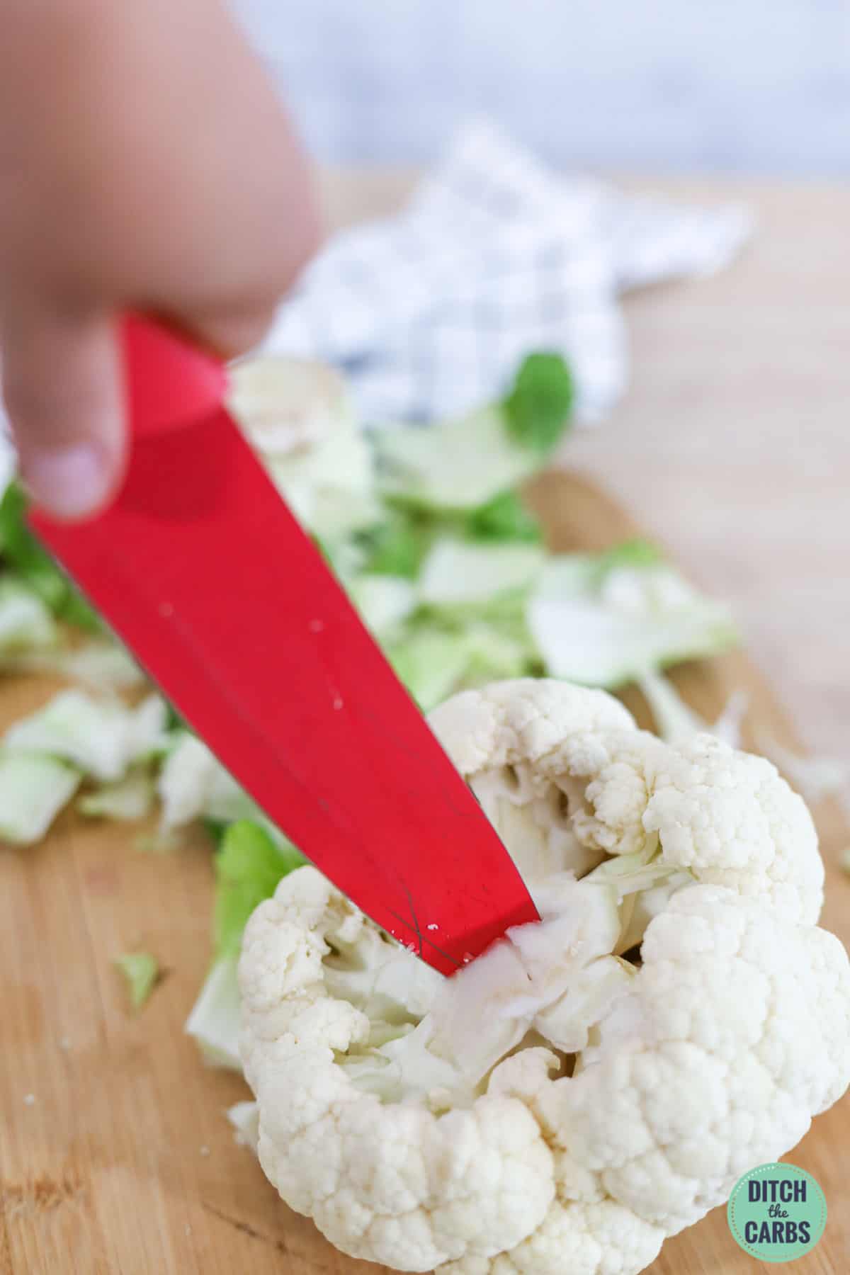 a red knife cutting into a whole cauliflower