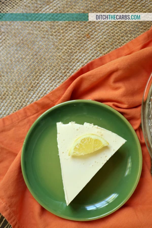 A plate of sliced lemon cheesecake on a orange cloth and garnished with a slice of lemon