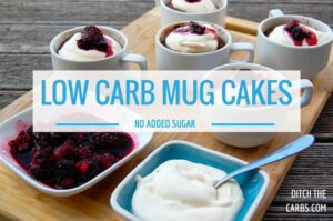A selection of mug cakes served in white mugs with whipped cream and fresh berry sauce