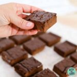 nut-free keto brownies cut into squares on a tray with a hand holding one