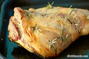 A close-up of roast lamb with fresh rosemary cooked in a roasting pan