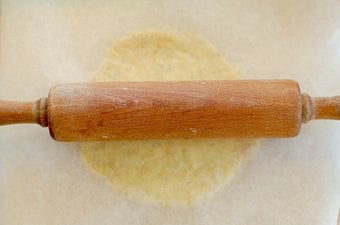 A wooden rolling pin making fat head pizza dough into a pizza shape