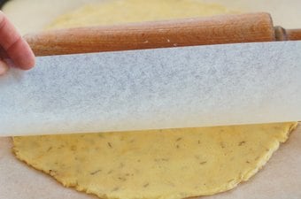 Low-carb pizza dough being rolled out with baking parchment and a wooden rolling pin