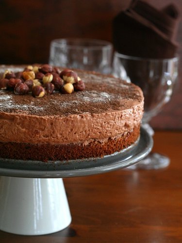 A piece of chocolate hazelnut cake sitting on top of a wooden table and cake stand