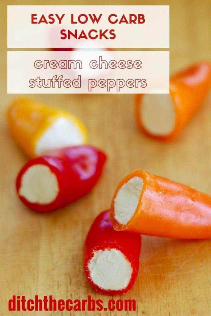 Mini peppers sliced in half and stuffed with cream cheese on a wooden chopping board