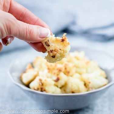 A person holding a cauliflower dipping in mayonnaise