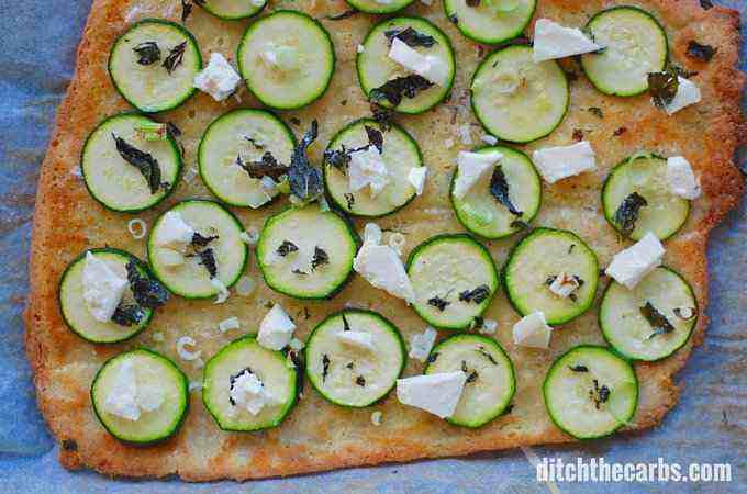 A pizza sitting on top of a wooden cutting board, with Courgette