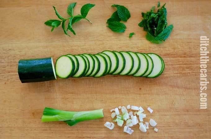 Sliced zucchini on a chopping board with herbs and onions