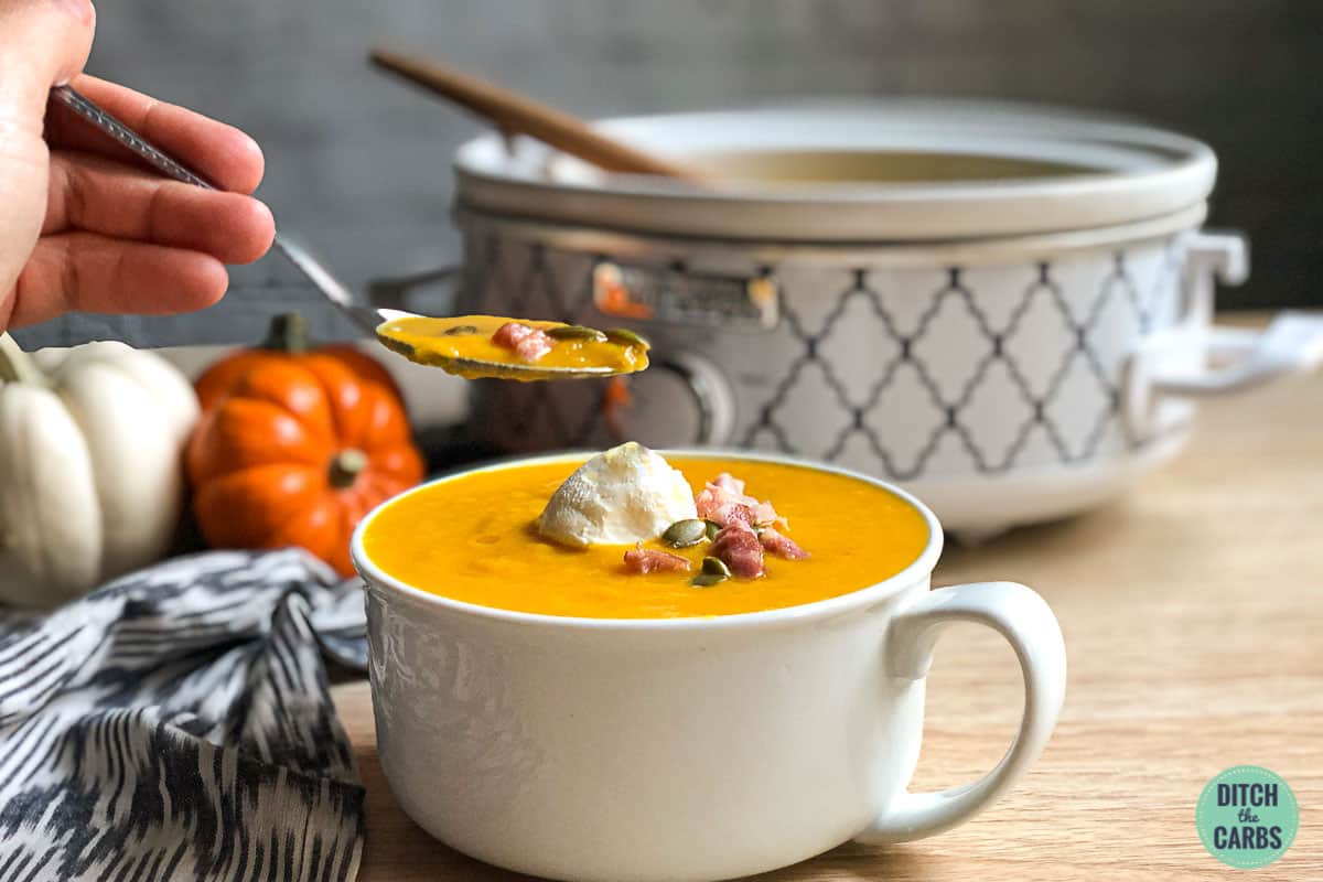 keto pumpkin soup in a white mug garnished with bacon and cream