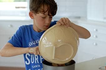 boy in a blue shirt pouring cake batter into a cake tin