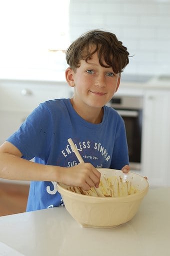 little boy in a blue shirt with a mixing bowl and wooden spoon