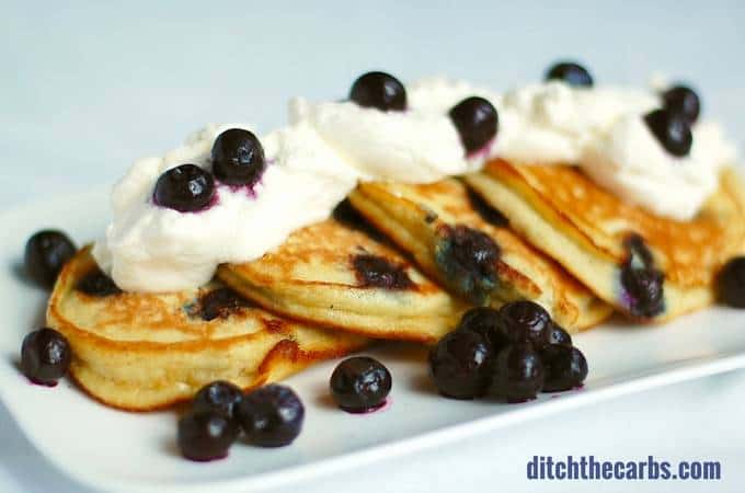 blueberry paleo pancakes served on a white dish with whipped cream and berries