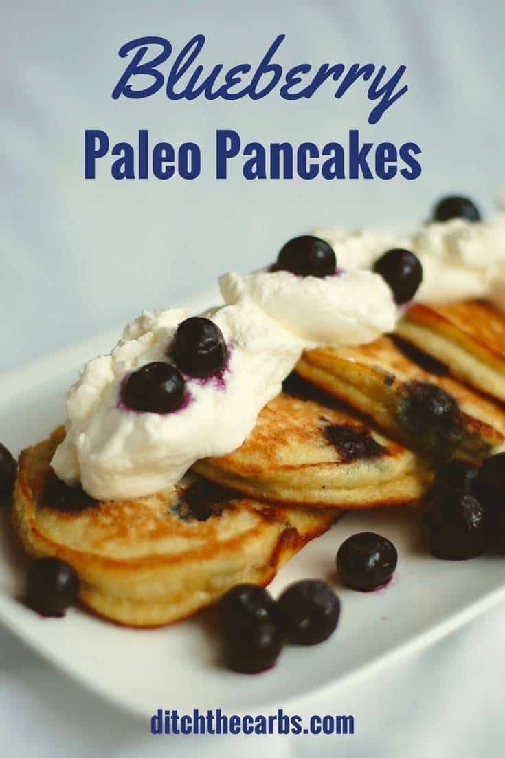 blueberry paleo pancakes served on a white dish with whipped cream and berries