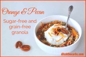 A bowl of gluten-free granola garnished with orange zest and pecans served with a silver spoon and yoghurt