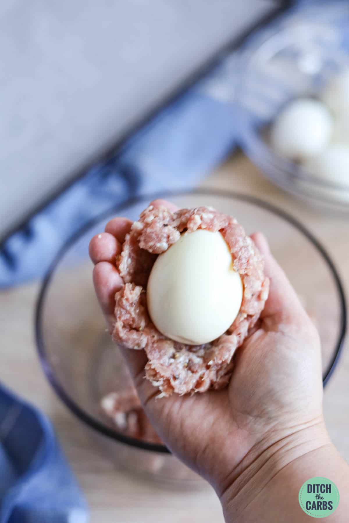 a boiled egg being wrapped in ground pork and herbs with seasoning to make a keto scotch egg
