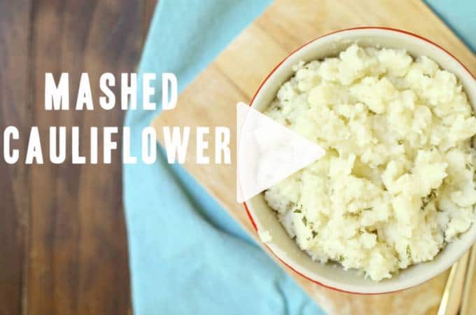 A red bowl full of mashed cauliflower sitting on a wooden board
