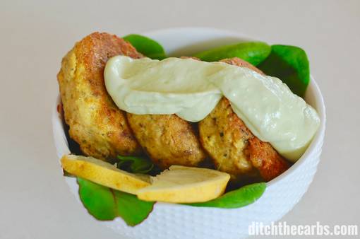 salmon patties with lime avocado dressing served in a white bowl with baby spinach