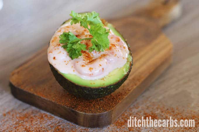 A slice of avocado sitting on top of a wooden cutting board stuffed with prawns