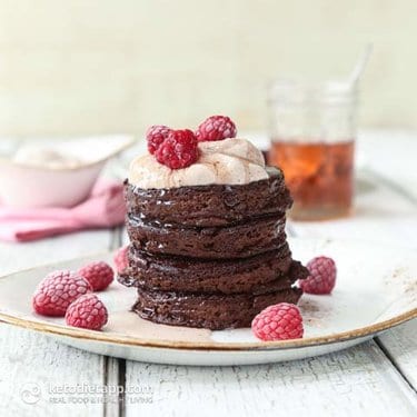 A stack of chocolate pancakes with berries and cream