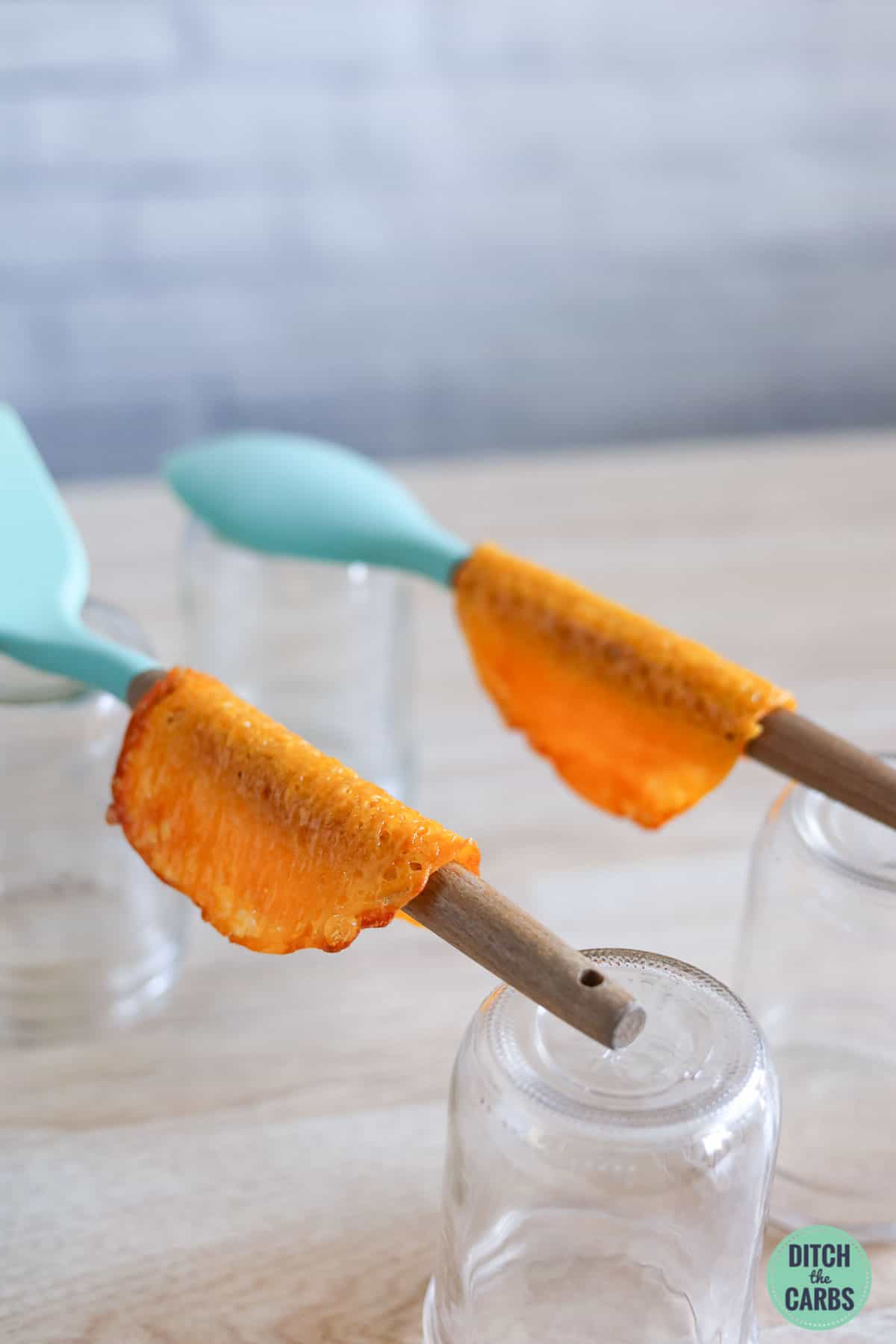 cheese taco shells sitting on two wooden spoons to make a taco shell shape