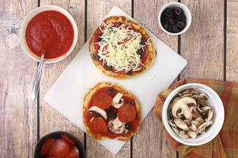 A bowl of food sitting on top of a wooden table, with pizza bases and toppings