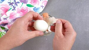 Two hands peeling a boiled egg
