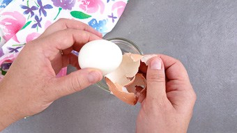 Two hands peeling boiled eggs