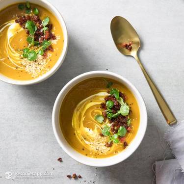 Two bowls of pumpkin soup garnished with herbs and bacon pieces