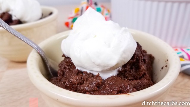 A bowl of chocolate dessert on a plate with whipped cream
