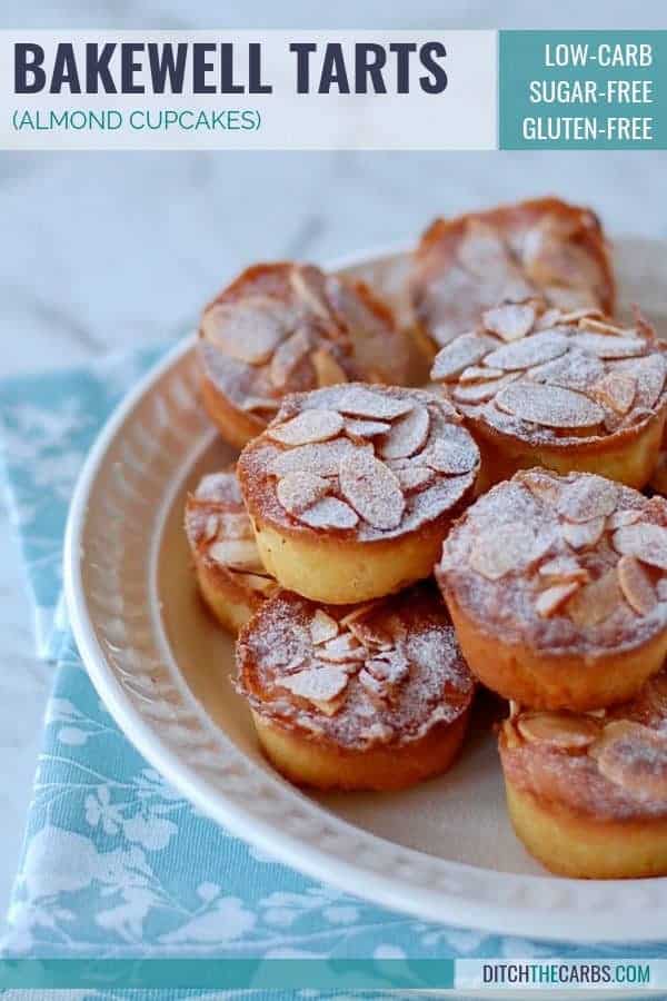 Almond cupcakes stacked on a white plate dusted with powdered sweetener 