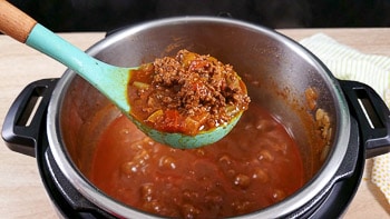 A bowl of chili being served with a blue ladle