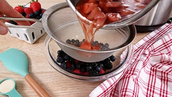 Draining the cooked berries into a sieve into a glass bowl