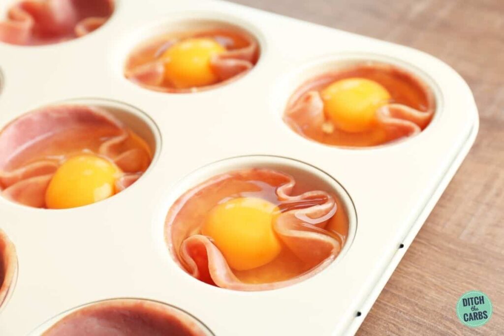 ham lined muffin tray with eggs cracked into each one