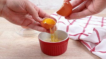 Hands breaking an egg into a red ramekin