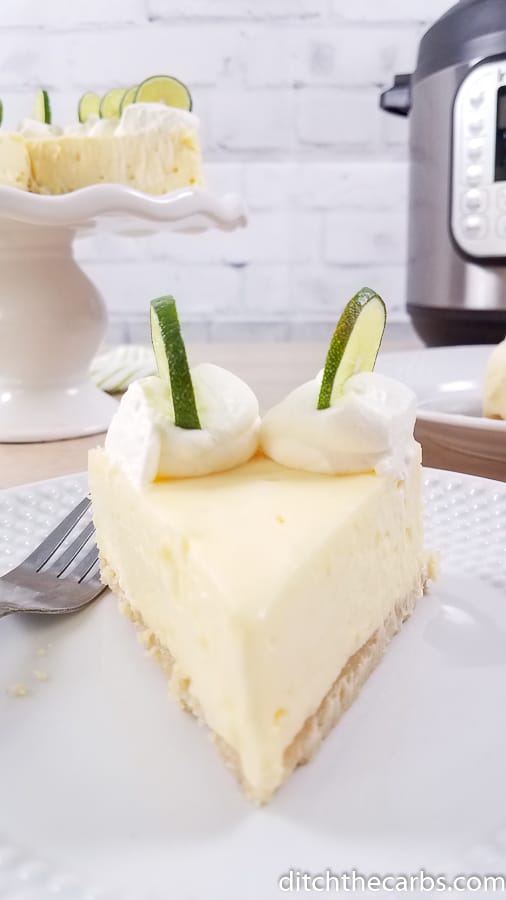sliced Instant Pot key lime cheesecake on a white plate with the Instant Pot in the background