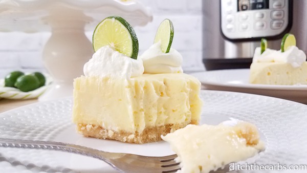 A slice of lime cheesecake in front of the Instant Pot and served with whipped cream