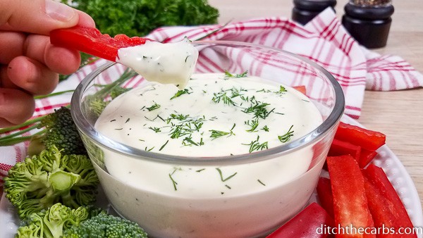 A bowl of magic one minute mayonnaise garnished with dill and been dipped with sliced peppers