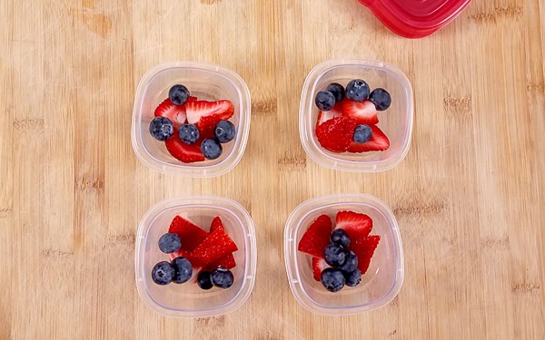 4 plastic pots with fresh berries on top of a wooden table