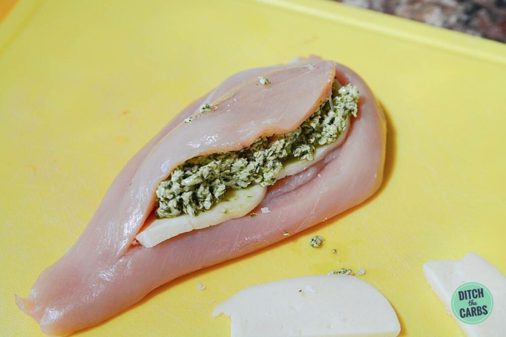 raw chicken breast being stuffed with cheese and pesto