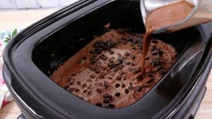 Pouring chocolate sauce onto the cake batter in the slow cooker