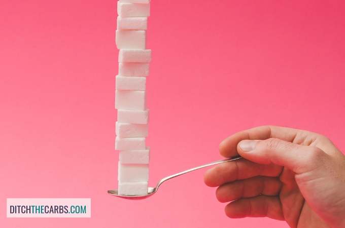 A man\'s hand holding a spoon stacked with sugar cubes